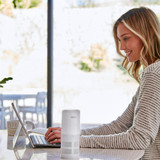 White | Woman smiling while typing on tablet next to the Homedics TotalClean 4-IN-1 UV Portable Air Purifier in white