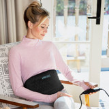 Woman sits on chair and adjusts settings on the LCD controller for the Homedics Women’s Health Abdomen and Lower Back Hot & Cold Gel Therapy Belt