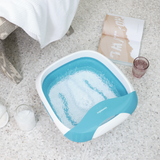Compact Pro Spa Collapsible Footbath with Heat next to soaking salts and a glass of water